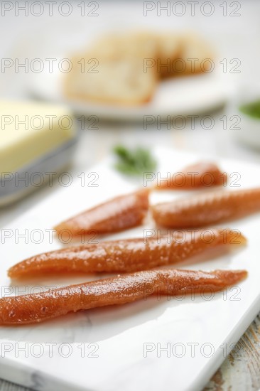 Herring caviar glisten with a rich color, artfully arranged on a marble platter. In the background, slices of butter and herbs hint at a culinary preparation