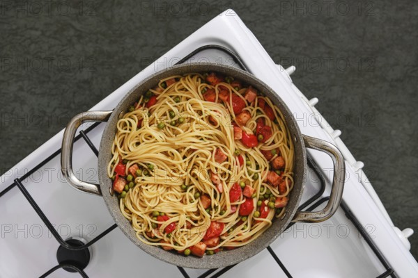 Overhead view of a pot filled with freshly cooked pasta with bacon and tomatoes on a stovetop. The inviting aroma fills the cozy kitchen as it prepares for a hearty meal in the afternoon