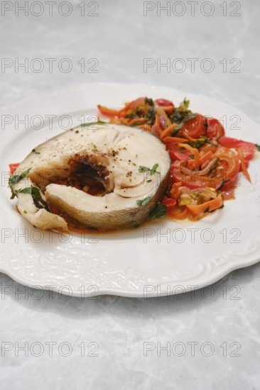 A generous portion of tender white fish is plated alongside a colorful mix of sautéed tomatoes and herbs