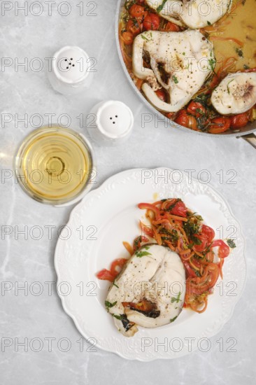 Tender cod fish fillet with colorful sautéed peppers, carrots and tomatoes on a plate on a dining table