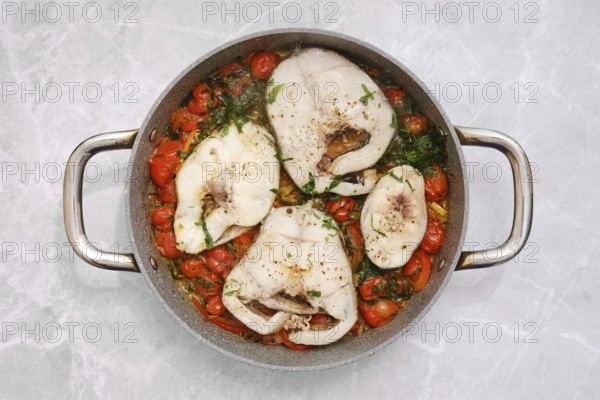 Cod fish fillets are gently simmering in a tangy tomato sauce, accompanied by vibrant cherry tomatoes and fresh herbs