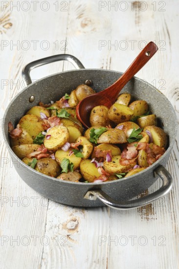 Golden-brown potatoes mixed with crispy bacon, fresh herbs, and onions are presented in a stovetop pot. The mouthwatering dish is garnished and waiting to be enjoyed for a hearty meal