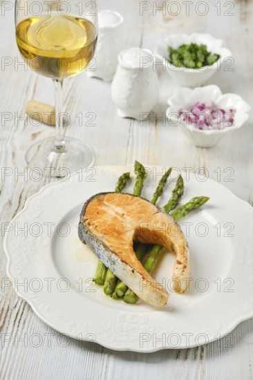 A succulent piece of salmon on a plate with crispy asparagus spears. Accompanying the dish is a glass of white wine. Small bowls of seasonings complete the table setting