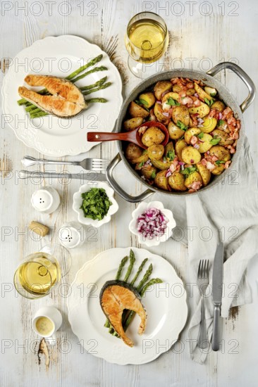 A beautifully arranged dining table features two plates of grilled salmon served with roasted potatoes and asparagus. Two glasses of white wine complete the elegant setting for a relaxing dinner