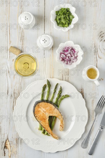 Grilled salmon and tender asparagus on a plate served for dinner. Bowls of chopped onion and herbs accompany a glass of white wine
