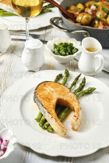 A perfectly cooked salmon steak rests on a bed of crispy asparagus. Accompanied by fresh herbs and a glass of white wine, this meal showcases elegant dining with gourmet flavors