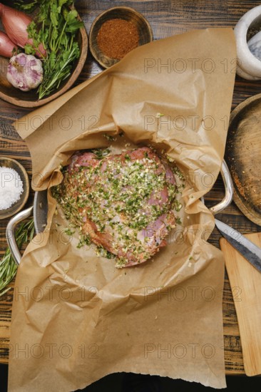 A seasoned turkey thigh in a pan lined with parchment paper, surrounded by fresh herbs, spices, and other ingredients. This cozy kitchen radiates warmth and culinary inspiration