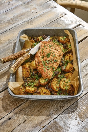 A succulent roasted turkey breast sits atop a bed of roasted golden potatoes, garnished with fresh herbs, creating a hearty meal on a rustic wooden table in a cozy setting