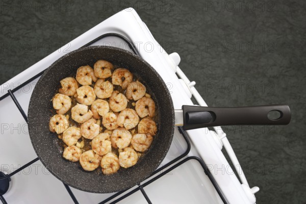 A frying pan on a stovetop filled with perfectly cooked shrimp in a kitchen. The shrimp are golden-brown and evenly spaced, revealing a delightful meal preparation underway