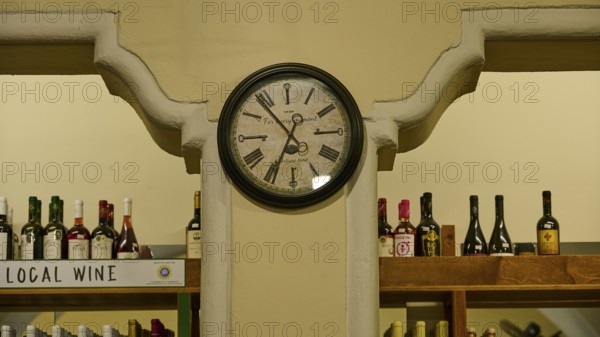Agora, Municipal Market Hall, An antique clock on the wall of a wine shop with filled shelves, Kos Town, Kos, Dodecanese, Greek Islands, Greece