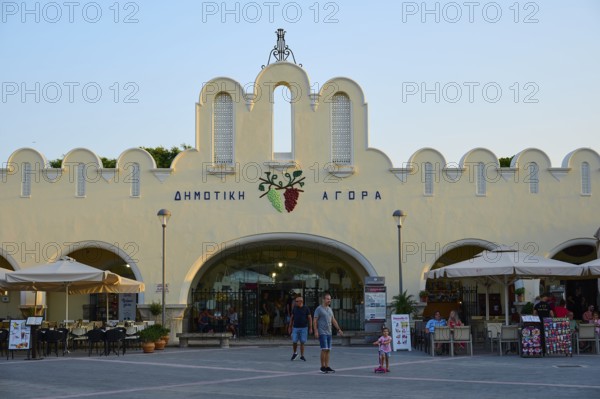 Agora, Municipal market hall, Lively market with white buildings and parasols in the foreground, Kos Town, Kos, Dodecanese, Greek Islands, Greece