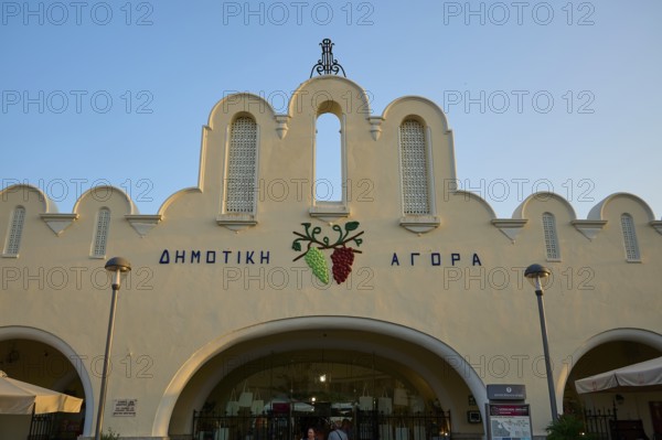 Agora, Municipal Market Hall, White market hall with Greek writing and grape emblem, illuminated by the evening sun, Kos Town, Kos, Dodecanese, Greek Islands, Greece