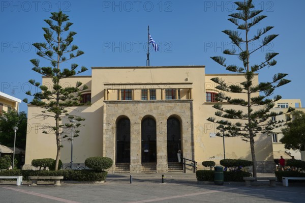 Archaeological Museum, Symmetrical beige building with Greek flag and tall trees, under clear sky in urban environment, Kos Town, Kos, Dodecanese, Greek Islands, Greece
