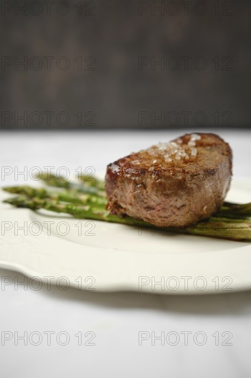Succulent filet mignon is perfectly cooked and garnished with a sprinkle of sea salt, placed on a bed of tender grilled asparagus on elegant white china, creating a sophisticated dining experience