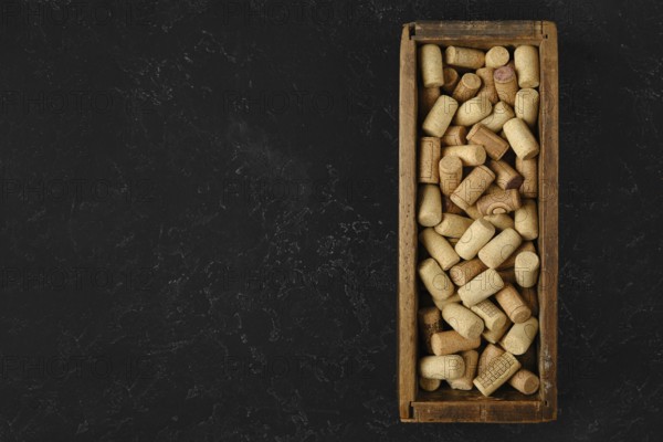 A wooden box filled with assorted wine corks rests on a dark surface. The corks vary in size and shape, showcasing a collection from different wine bottles, hinting at past wine tastings