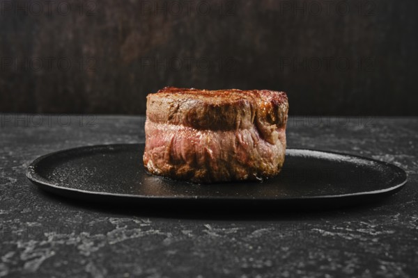 A perfectly cooked filet mignon rests on a sleek black plate, showcasing its rich color and delicate texture