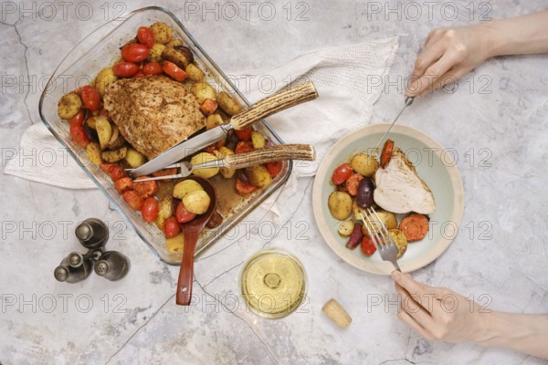 Tender roasted turkey breast rests in a baking dish surrounded by vibrant roasted vegetables. A person prepares to eat a slice alongside assorted veggies, embodying a warm, inviting meal