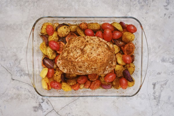 Juicy turkey breast seasoned with spices rests atop a bed of roasted baby potatoes, cherry tomatoes, and carrots. The dish is oven-cooked for a flavorful and colorful meal ready to serve