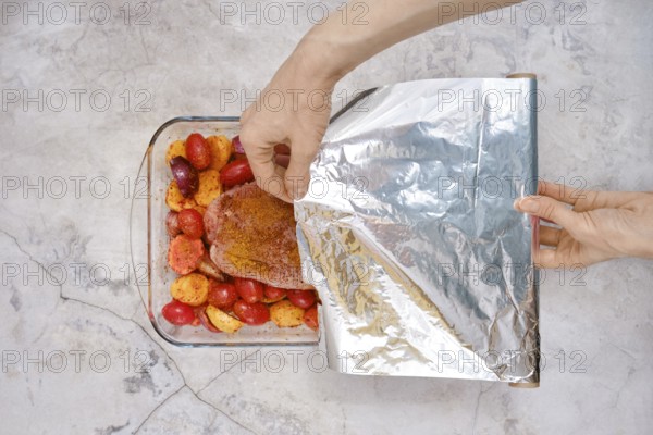 A hand gently covers a baking dish filled with seasoned turkey breast and juicy vegetables with foil ready to cook