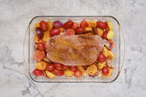 A perfectly seasoned turkey breast rests on a bed of vibrant potatoes, tomatoes and onion ready to be roasted