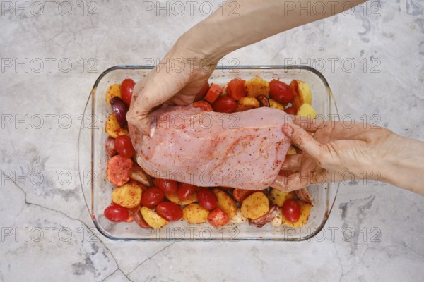 Hands carefully place a raw turkey breast onto a bed of seasoned potatoes and tomatoes