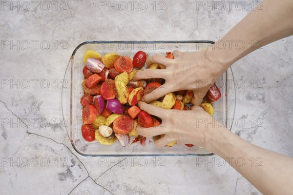 Hands mix together seasoned potatoes, tomatoes, and onions in a glass dish for a turkey breast recipe