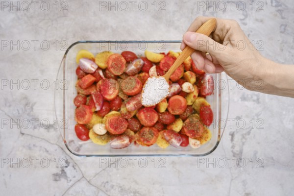 A hand sprinkles salt over colorful fresh vegetables and seasonings, preparing a vibrant mix to accompany a turkey breast in a glass baking dish. The setting is bright and inviting