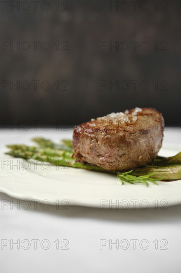 A perfectly cooked filet mignon, seared to golden brown, sits on a decorative plate alongside tender asparagus. The dish is presented in an elegant setting, emphasizing gourmet dining experience
