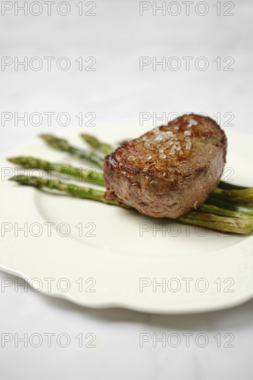 Filet mignon is grilled to perfection and presented on a white plate atop freshly cooked asparagus. A sprinkle of sea salt enhances the flavors, creating an elegant and appealing dish