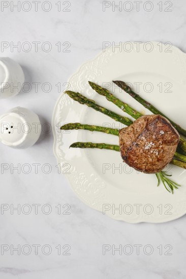 A perfectly cooked filet mignon sits elegantly on a white plate alongside vibrant asparagus spears. The meal is seasoned simply, enhancing its natural flavors and appeal