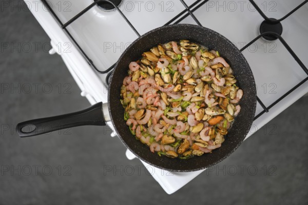 Seafood stir-fry with shrimp and mussels in a black pan, mixed with colourful herbs and spices on a gas stove, overhead view