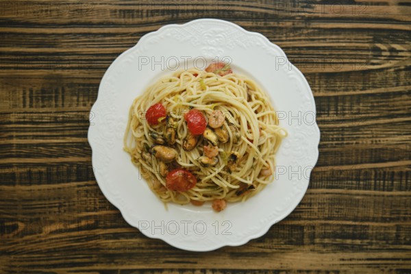 A generous serving of spaghetti topped with an assortment of seafood, including shrimp and mussels, garnished with fresh cherry tomatoes and herbs, elegantly presented on a white plate