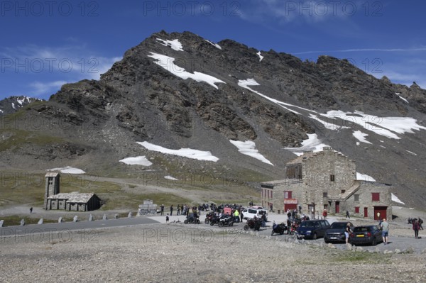 View of pass summit from pass road alpine road mountain road highest passable 2764 2770 metre high alpine pass Col de l'Iseran, in the foreground car park, on the left chapel Notre-Dame-de-Toute-Prudence. on the right building with restaurant, in the background 3041 metre high mountain peak Pointe des Lessières, Col de l'Iseran, department road D902, Route des Grandes Alpes, Département Savoie, Region Auvergne-Rhône-Alpes, Graian Alps, France