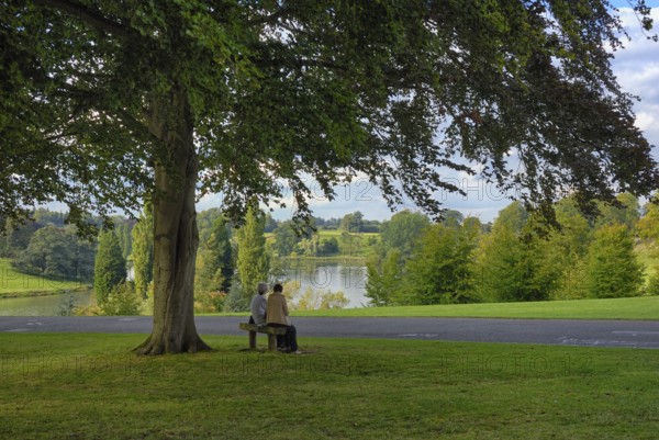 Two woman on a bench in the park of Blenheim Palace, the largest non-royal aristocratic residence in Great Britain, built by Queen Anne as a reward for John Churchill, 1st Duke of Marlborough. The imposing baroque palace is located in the English county of Oxfordshire on the River Glyme, a UNESCO World Heritage Site, England, United Kingdom
