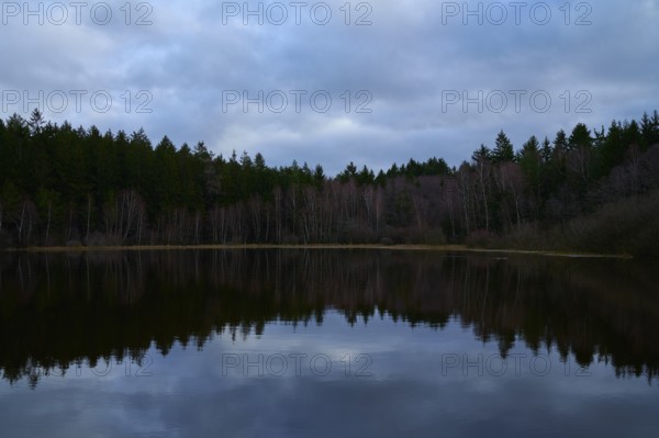 A calm lake in the evening with clouds and a beautiful reflection, surrounded by a forest, Mülbenersee, Mülben, Odenwald, Baden-Württemberg, Germany