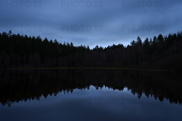 A quiet night scene with dark forest and reflection in the still water of a lake, Mülbenersee, Mülben, Odenwald, Baden-Württemberg, Germany