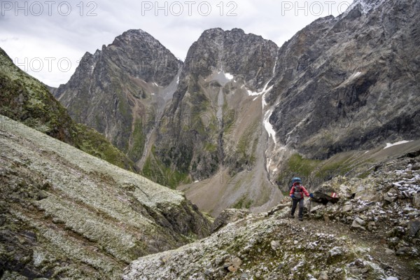 Mountaineer on steep rocky mountain landscape with fresh snow in summer, behind mountain peaks Großer Friedrichskopf and Georgskopf, ascent to Hornscharte, Schober group, Hohe Tauern National Park, Carinthia, Austria