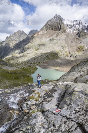 Mountaineer on a rocky hiking trail, view of the turquoise-blue mountain lake Großer Gradensee, behind her the summit of the Petzeck, Hoher Perschitzkopf and Kruckelkopf, Schober Group, Hohe Tauern National Park, Carinthia, Austria