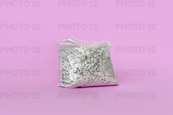 Small plastic bag containing ash of a pet cat after cremation on pink background
