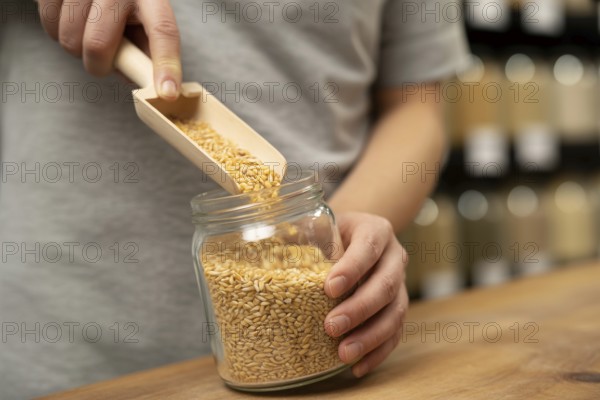 Person filling small glass jar with grains using wooden scoop at bulk store. Concept of zero-waste and sustainable shopping. Generative Ai, AI generated