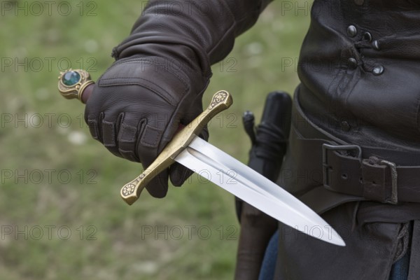 Hand in leather glove holding medieval dagger with gemstone. Concept of authentic medieval or LARP cosplay. Generative ai, AI generated