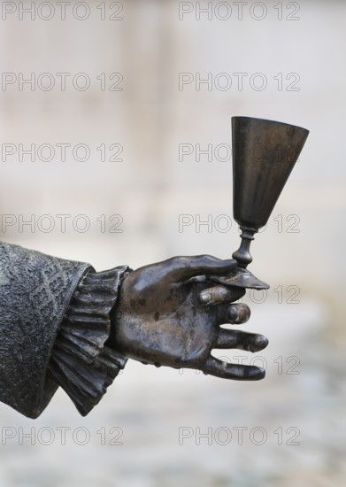 Close-up of hand holding champagne glass, statue of Louis XV in front of Hotel Champagne De Venoge, Épernay, Champagne, Marne, France