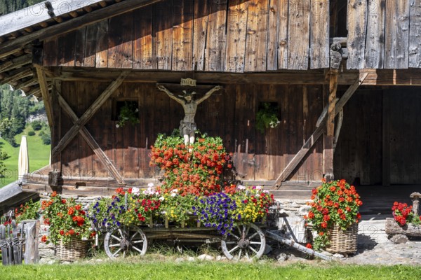Colourful floral decorations and crucifix at a rustic alpine hut, Ridnauntal, South Tyrol, Italy