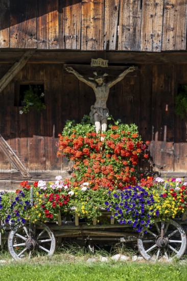 Colourful floral decorations and crucifix at a rustic alpine hut, Ridnauntal, South Tyrol, Italy