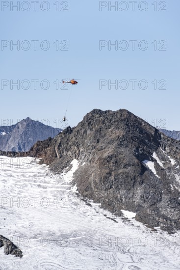 Helicopter with a load on a rope flies over glaciers and mountains, Stubai Alps, South Tyrol, Italy