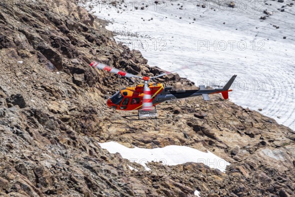 Red helicopter flies over glaciers in the mountains, Stubai Alps, South Tyrol, Italy
