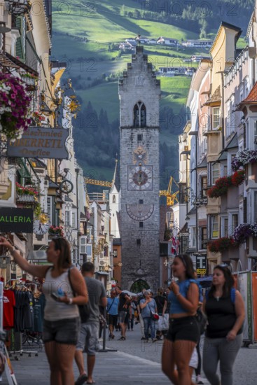 Tourists in the old town, colourful houses in the main street, Zwölferturm tower at the back, Sterzing, South Tyrol, Italy