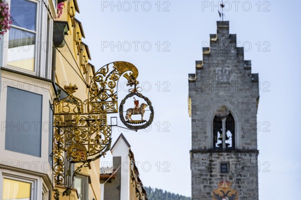 Artistic golden hanging sign, nose sign, old town centre, behind Zwölferturm, Sterzing, South Tyrol, Italy