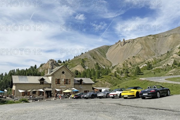 View of historic inn Refuge Napoleon on north ramp northern ascent downhill mountain road in front of pass summit of Alpine pass road Col d'Izoard, in front of it on the right many Porsche sports cars, Col de l'Izoard, Cottian Alps, Route des Grandes Alpes, Département Hautes-Alpes, France