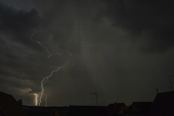 Dark clouds gather as lightning strikes light up the night above the rooftops. The intense storm brings thunder and rain to the quiet neighbourhood below. Bas rhin, Alsace, grand est, France